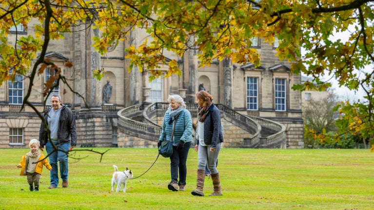 Adults and children walking a dog in autumn with Kedleston Hall behind them